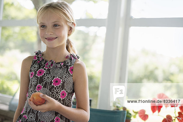 A young girl in a floral dress holding a peach fruit.