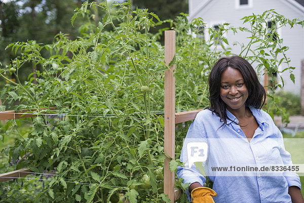 A woman working in the garden. Leaning on a fence smiling.