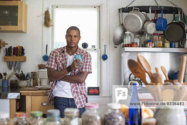 Ein Mann mit einem Getränk in der Hand steht in einer Bauernküche.