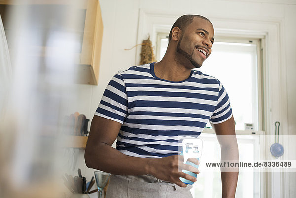 Ein Mann in einer Bauernküche  der ein Getränk in einem blauen Glas hält.