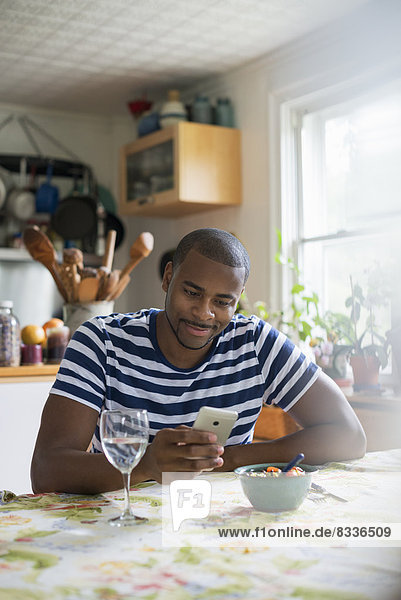 A man sitting at a table using a smart phone. Fruit dessert and a glass of wine at hand.