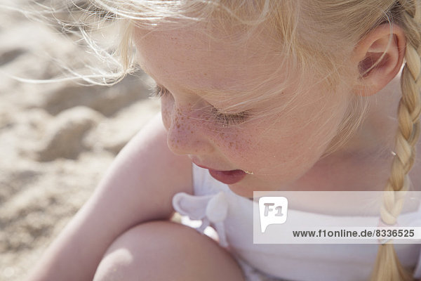 Ein junges Mädchen mit blonden Haaren in Zöpfen am Strand.