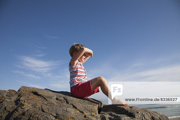 Ein Kind sitzt auf den Felsen und schaut aufs Meer hinaus.