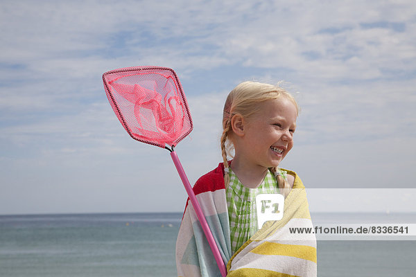 Ein junges Mädchen mit einem Strandtuch um die Schultern  das ein kleines Fischernetz trägt.