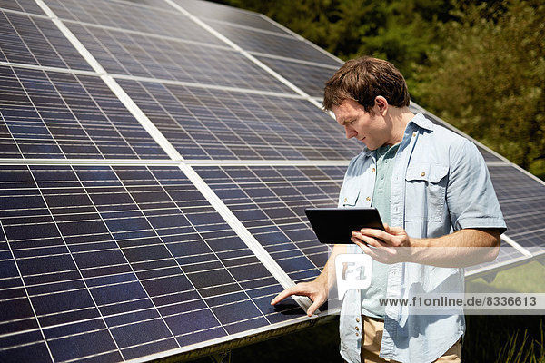 Ein Landwirt  der die Oberfläche eines Solarpanels auf dem Bauernhof genau inspiziert.
