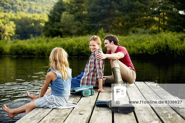 Drei Personen  zwei Erwachsene und ein Kind  die sich auf einem Steg entspannen  mit den Füßen im Wasser am Ende eines Tages.