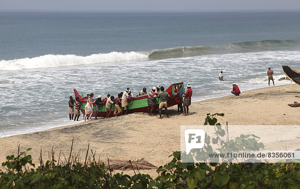 Fischer schieben ihr Boot aus dem Wasser an den Strand  Varkala  Kerala  Indien