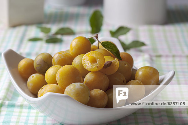 Mirabelles (Prunus domestica subsp. syriaca) in a bowl on wooden table  studio shot