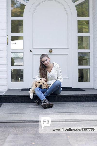 Teenage girl with dog sitting in front of an entry door