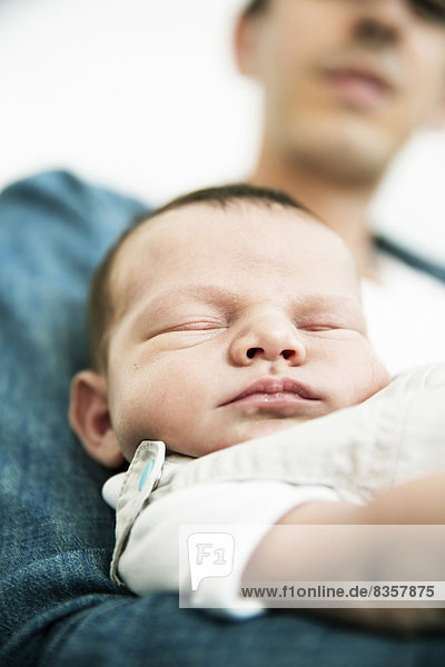 Junger Vater hält seinen schlafenden  neugeborenen Sohn in der Hand