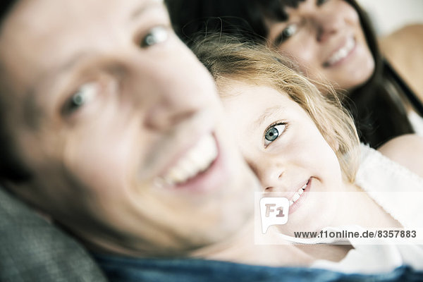 Lächelnde junge Eltern mit kleiner Tochter auf dem Sofa zu Hause  Nahaufnahme
