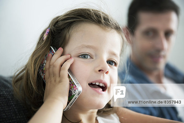 Portrait of little girl phoning with cellular  her father watching her