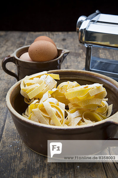 Ungekochte Tagliatelle und Eier auf Holztisch
