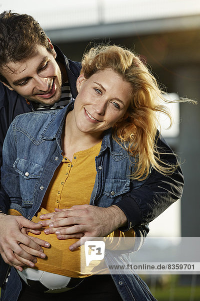 Junges Paar umarmt  Frau versteckt Ball unter dem Hemd