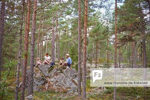 Family sitting on rocks in forest eating picnic