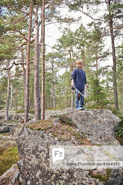 Boy standing on rocks holding stick