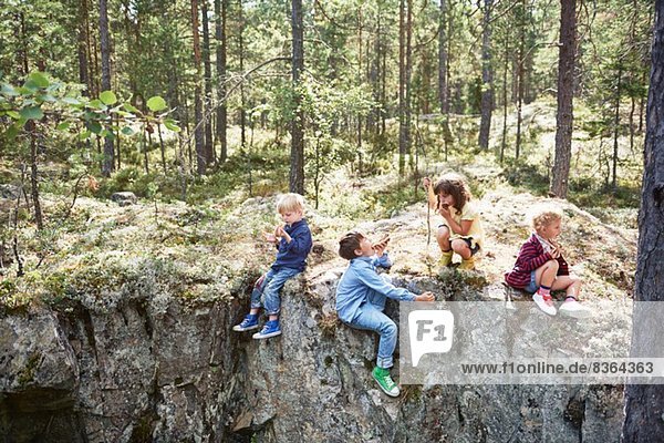 Kinder sitzen auf Felsen im Wald und essen Picknick