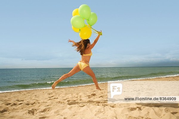 Frau springt mit Luftballons am Strand