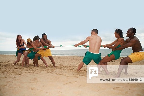 Friends playing tug of war on beach