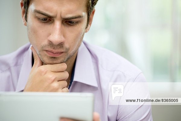 Junger Mann betrachtet Nachricht auf digitalem Tablett