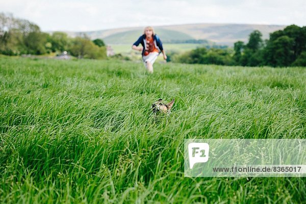Junger Mann und sein Hund rennen durchs Grasfeld
