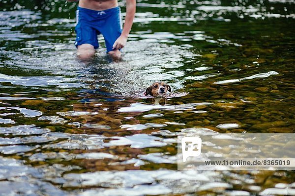 Junger Mann und sein Hund schwimmen im Fluss