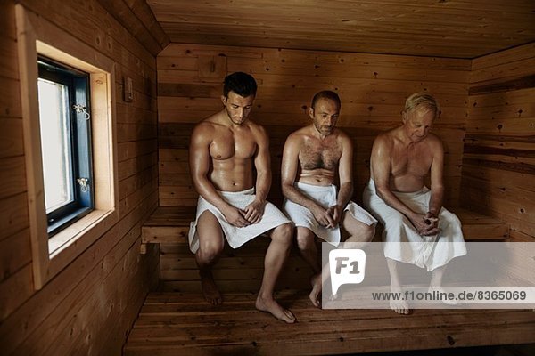 Drei Männer sitzen in der Sauna mit gebeugten Köpfen.