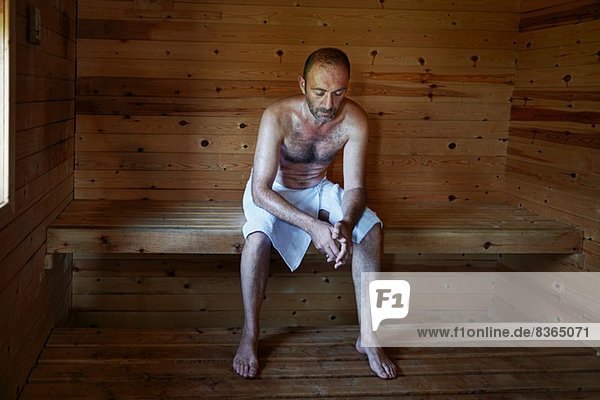 Der reife Mann entspannt sich in der Sauna mit dem Kopf nach unten.