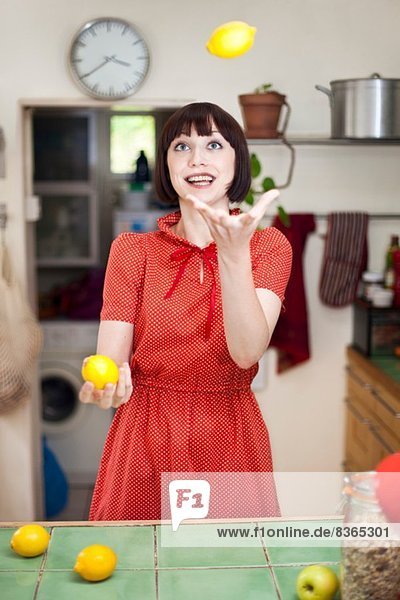 Junge Frau in der Küche jongliert mit Zitronen