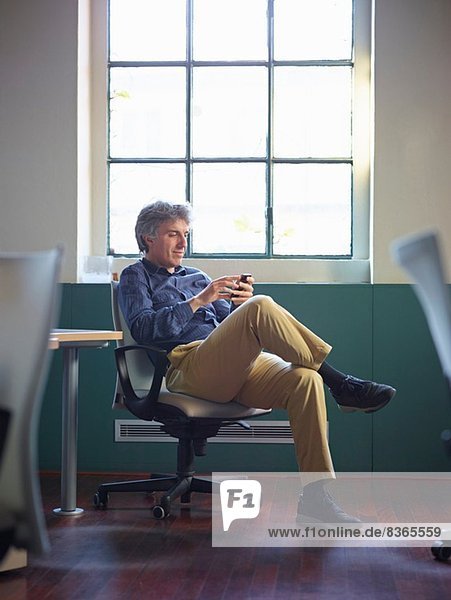 Mature businessman sitting on office chair wit cell phone