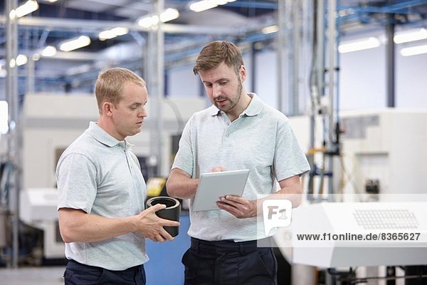 Two workers looking at digital tablet in engineering warehouse