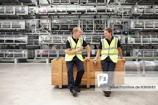 Two warehouse workers leaning on crate in engineering warehouse