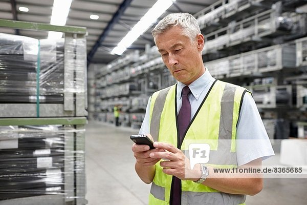 Portrait of manager using mobile phone in engineering warehouse