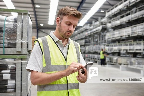 Portrait of worker using mobile phone in engineering warehouse