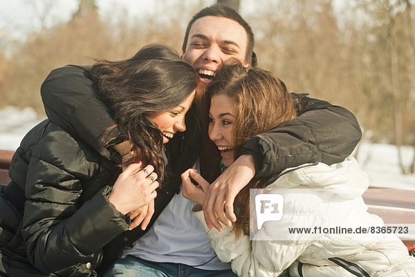 Drei junge Erwachsene  die sich im Winter auf der Parkbank umarmen
