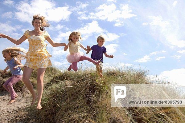 Mutter mit drei Kindern  die von den Dünen springen  Wales  UK