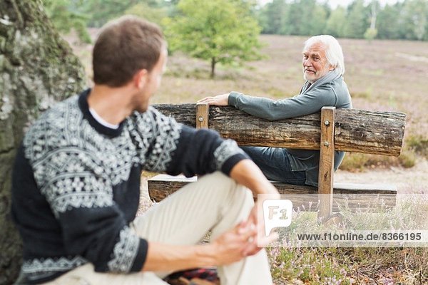 Senior man sitting on bench talking to mid adult man