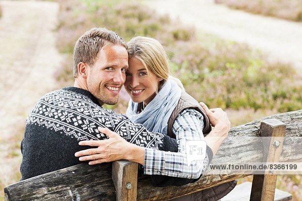 Mittleres erwachsenes Paar auf Holzbank mit Blick auf die Kamera