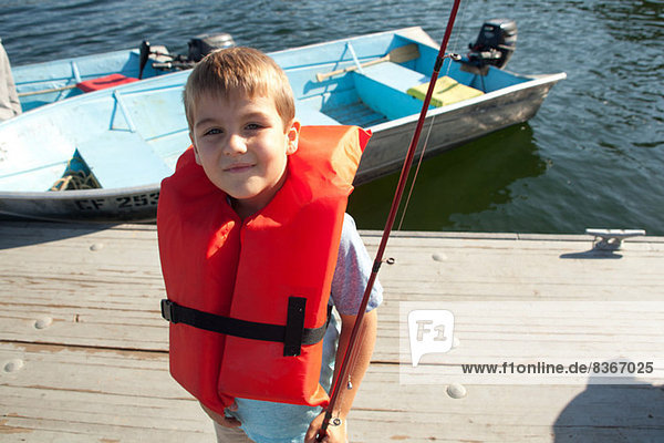 Boy in life jacket posing with fishing rod