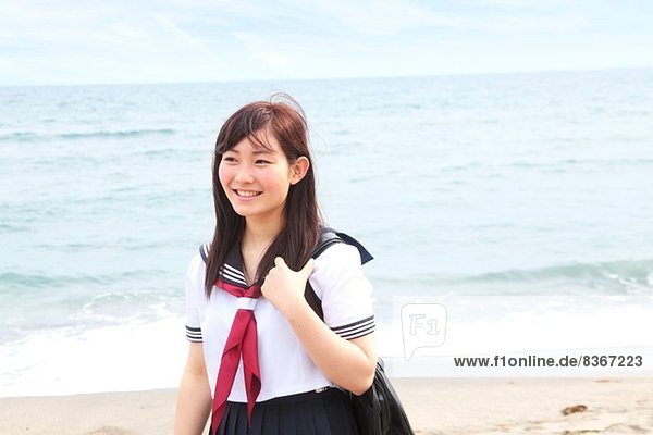 Junge Frau in Schuluniform am Strand stehend