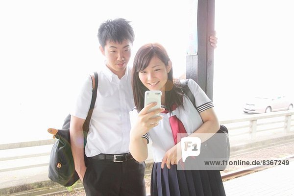 Junges Paar auf Bahnsteig mit Blick auf Smartphone
