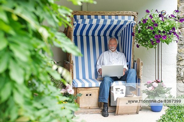 Senior Mann mit Laptop auf dem Gartensitz