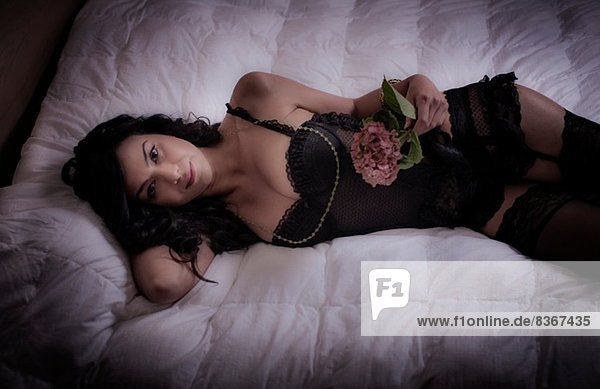 Mittlere erwachsene Frau  die auf dem Bett liegt und eine Blume hält.