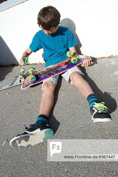 Teenage boy sitting on ground preparing skateboard
