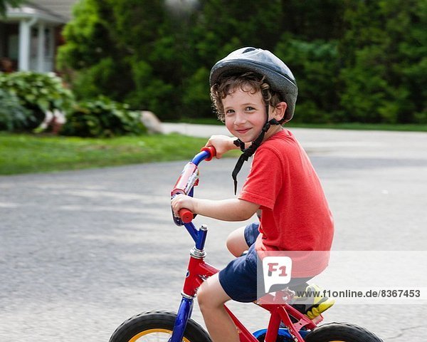 Porträt eines kleinen Jungen,  der mit dem Fahrrad auf der Einfahrt fährt