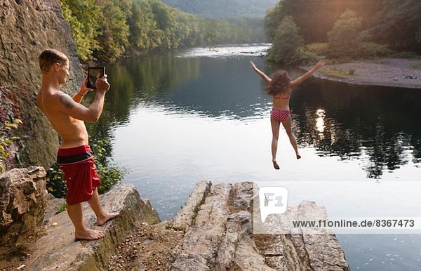 Young couple photographing jump from rock ledge  Hamburg  Pennsylvania  USA