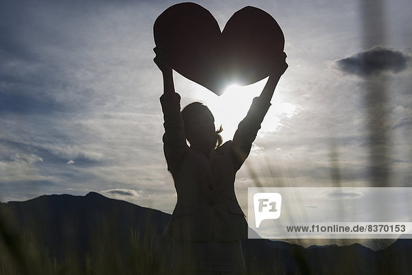 Silhouette Of A Woman Holding Up A Large Heart Shape Against The Sunlight