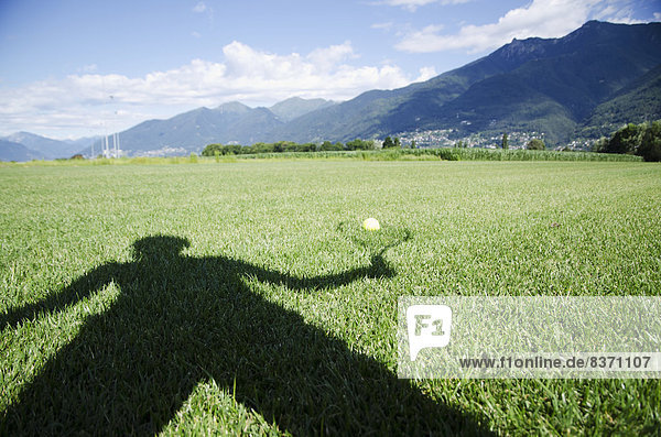 Shadow Of A Person Holding A Racquet Being Cast Onto A Ball Sitting On The Grass Locarno  Ticino  Switzerland