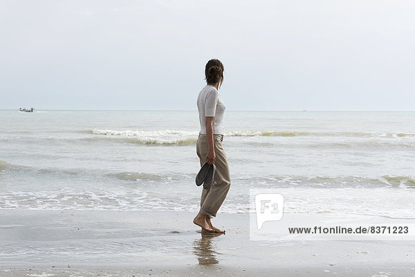 A Woman Walking On The Wet Beach Carrying Her Shoes And Looking Out At The Ocean Rimini  Emilia-Romagna  Italy