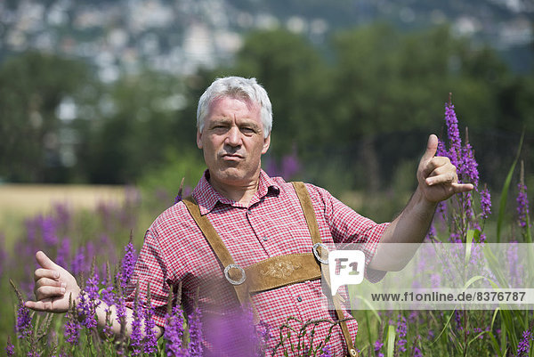 A Man Standing In A Field With Purple Blossoms Giving The Shaka Sign With His Hands  Locarno  Ticino  Switzerland